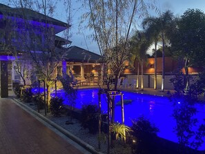 A pool area with a lounge chair and a dining table, surrounded by plants and a building with a sloped roof. - Lets Chill Pool Villa Najomtien Sattahip (Sattahip)