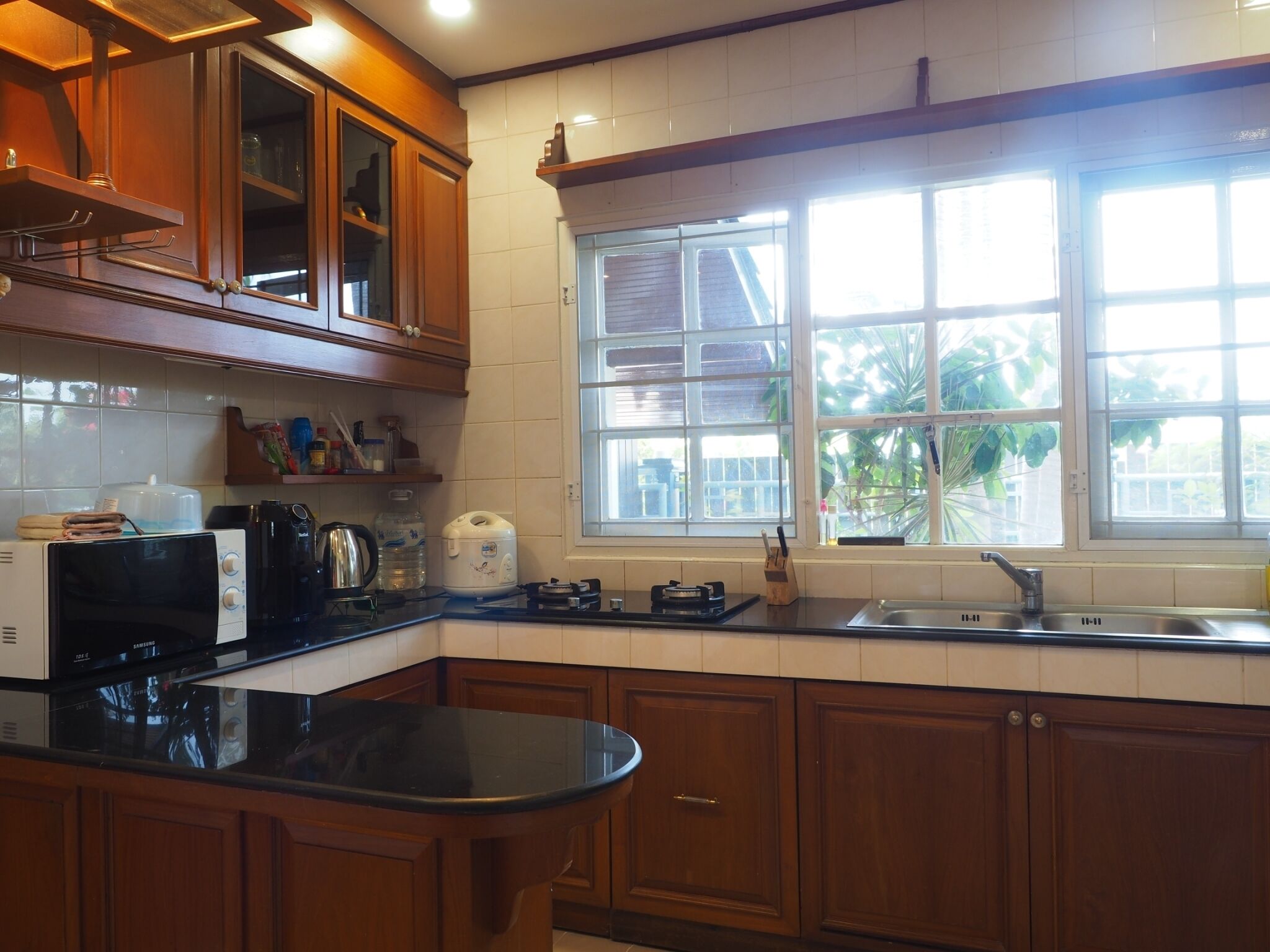 Una cocina con armarios de madera, microondas, tetera y ventana con vistas a zonas verdes.