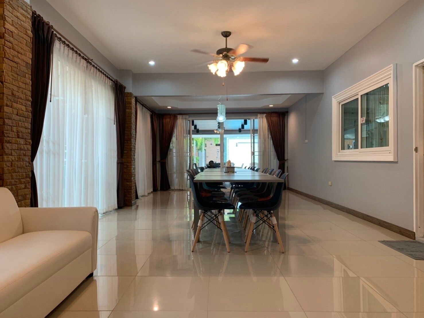 A spacious living room with a large dining table, a sofa, and a ceiling fan.