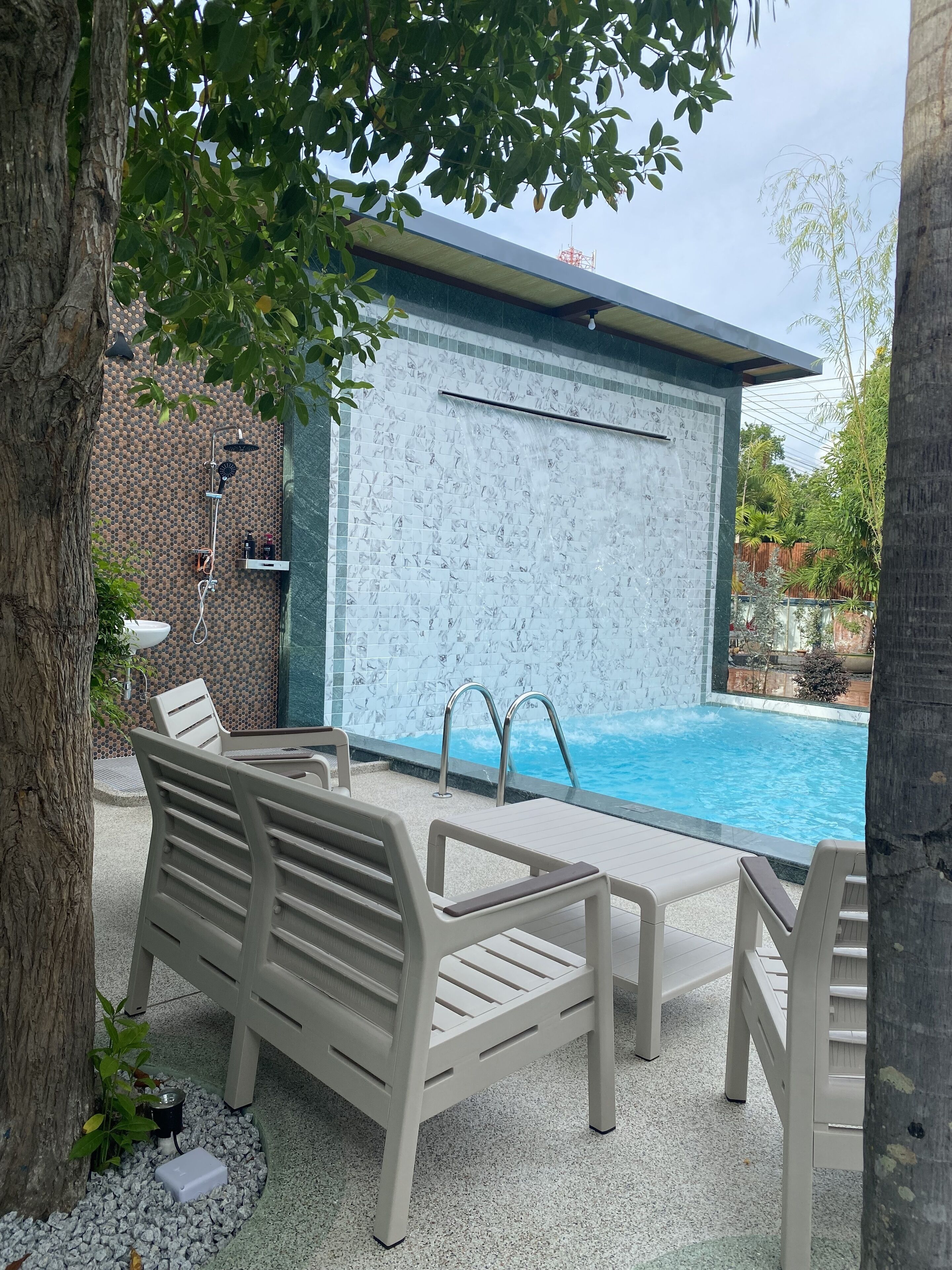 Een zwembadgedeelte met een betegelde muur, een jacuzzi en ligbedden.