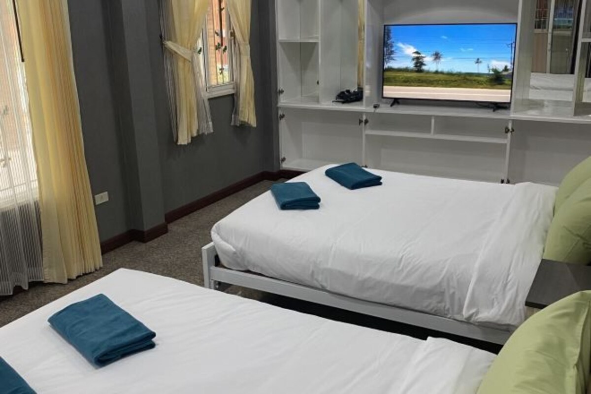 A hotel room with two beds, a TV on the wall, and a window with curtains.