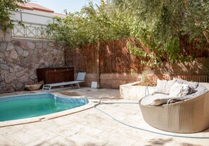 A backyard with a swimming pool, a wicker sofa, and a wooden deck.