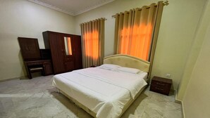A bedroom with a large bed, a wardrobe, a mirror, and curtains. - Super OYO 149 Bait Al Ghubaira Furnished Flat (Salalah)