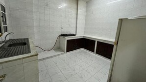 A small, tiled kitchen with a sink, a countertop, and a refrigerator. - Super OYO 149 Bait Al Ghubaira Furnished Flat (Salalah)