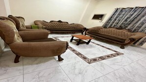 A living room with a brown sofa set, a brown armchair, and a patterned rug. - Super OYO 149 Bait Al Ghubaira Furnished Flat (Salalah)