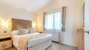 Une chambre à coucher avec un lit, des tables de chevet, un radiateur et une fenêtre avec des rideaux.