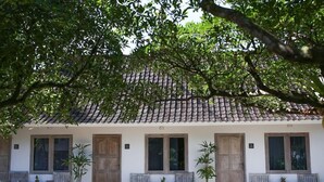 Un edificio con tejado de tejas, puertas y ventanas de madera. Hay bancos y plantas en macetas al frente.