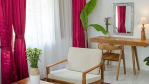 Una habitación con un escritorio de madera, una silla, una mesita pequeña y una planta grande.