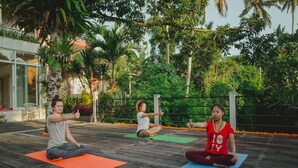 Tres personas practicando yoga sobre esterillas en una terraza de madera rodeada de abundante vegetación y palmeras.