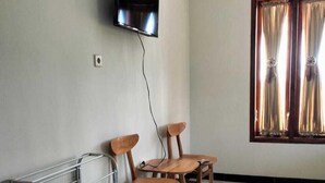 Una habitación con televisión de pantalla plana en la pared, una ventana con cortinas y un estante de metal con sillas.