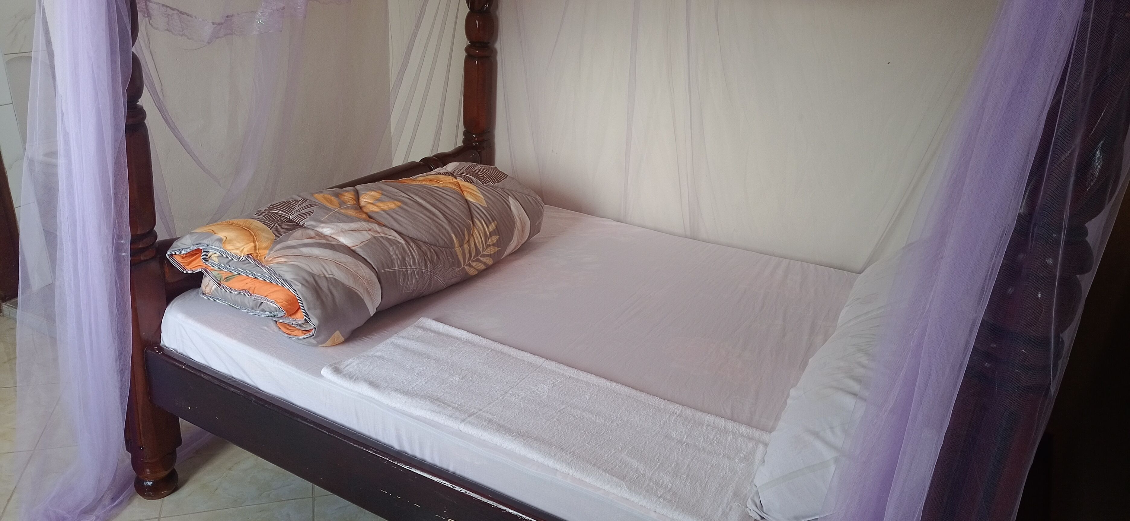 A single bed with a white mattress and a grey and orange patterned pillow.