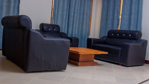 Una sala de estar con dos sofás de cuero negro, una mesa de centro de madera y cortinas azules.