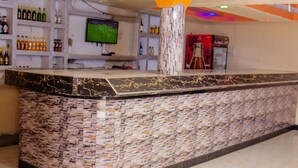 Una zona de bar con mostrador de mármol, estanterías con botellas, un televisor y un pilar con documentos.