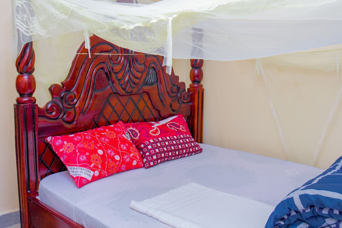Una cama con cabecera de madera, mosquitero y dos almohadas rojas con estampado floral.
