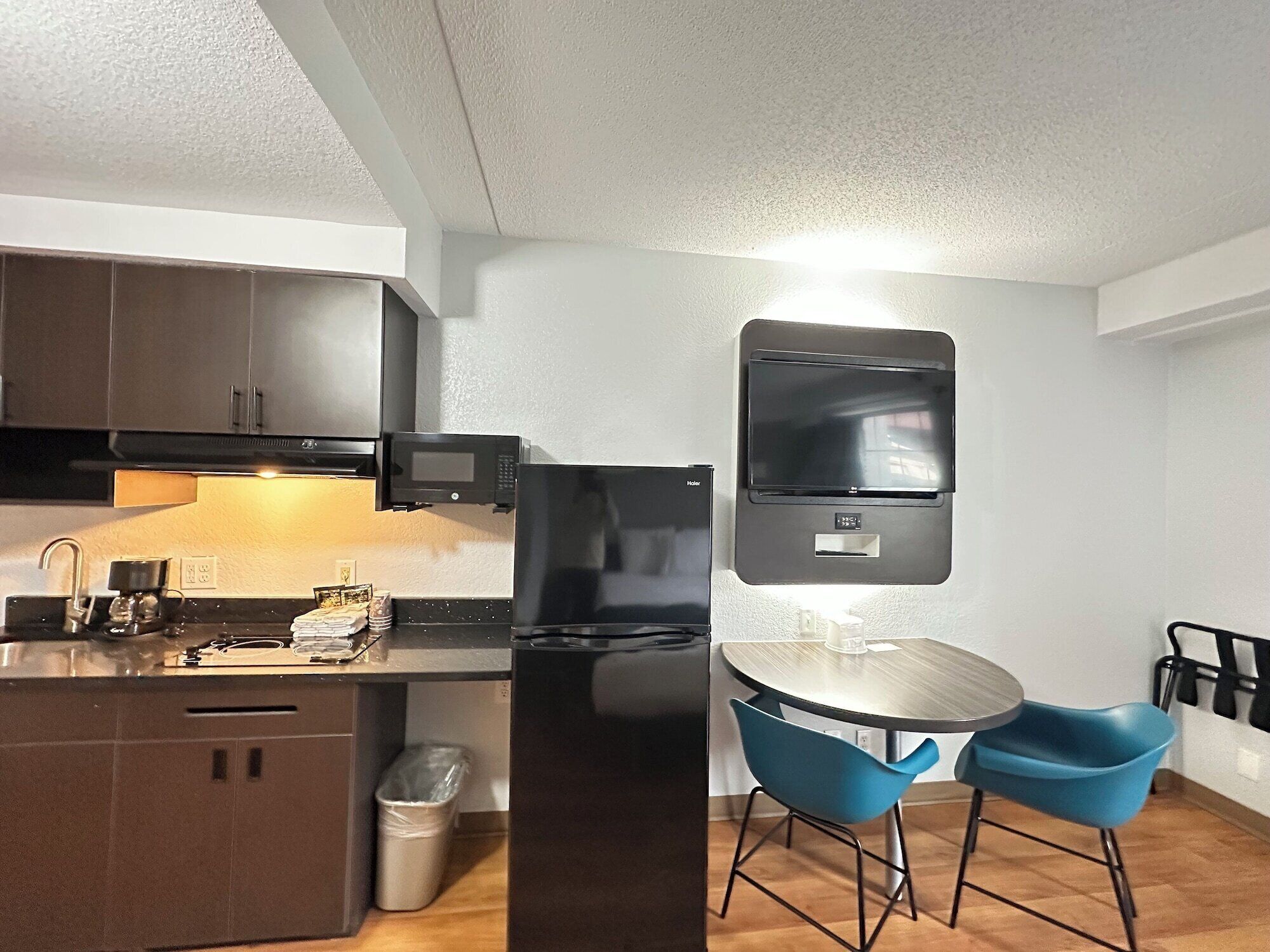 A compact kitchen with a microwave, stove, and a small refrigerator. There is a dining table with two chairs and a hanging rack above it.