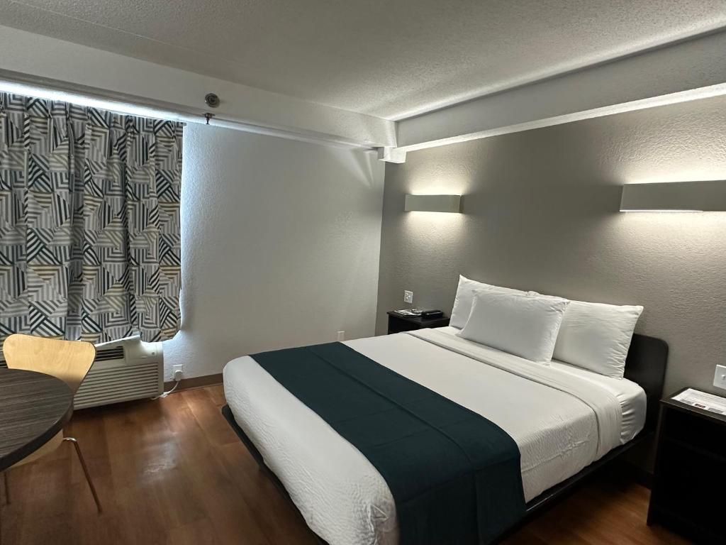 A hotel room with a bed, bedside tables, a desk, and a window with curtains.