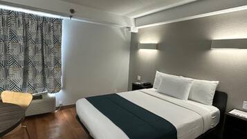 A hotel room with a bed, bedside tables, a desk, and a window with curtains.