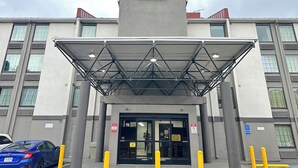 Edificio de Motel & Studio con entrada cubierta, señales de estacionamiento y un coche azul estacionado al frente.