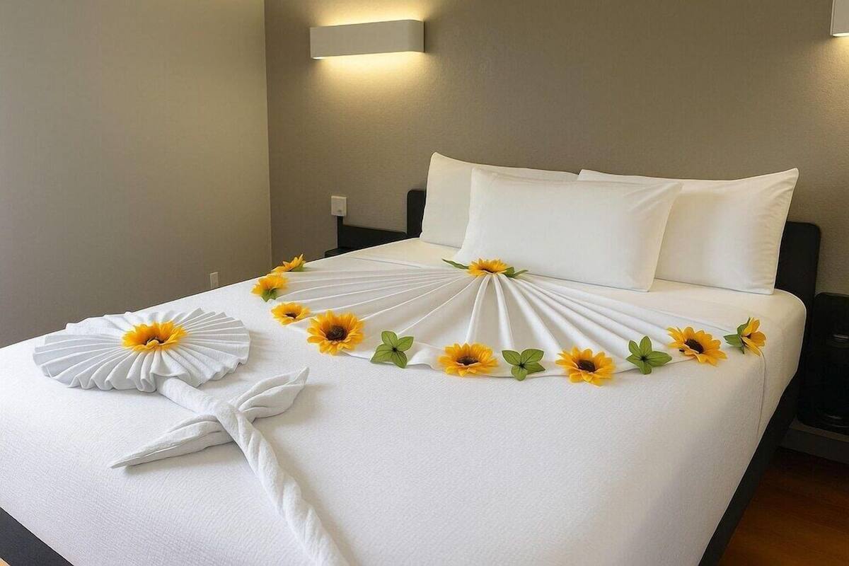 A neatly made bed with white linens, sunflowers, and a white fan decoration.