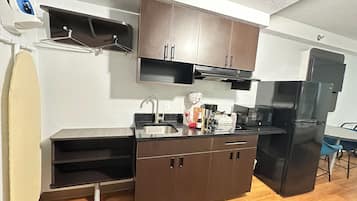 Una cocina compacta con armarios oscuros, un lavamanos de acero inoxidable y un refrigerador negro.