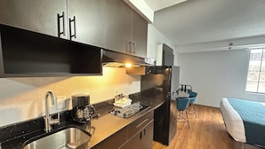 Cocina compacta con lavamanos, cafetera y refrigerador. Cuenta con un pequeño comedor con mesa y sillas.