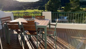 A wooden deck with a table and chairs, overlooking a green landscape and hills. - Renovated apartment with beautiful view of the beach golf course 5 minutes away (IB)