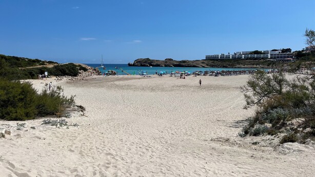 A beach with a sandy shore, a few people, and a building in the background. - Renovated apartment with beautiful view of the beach golf course 5 minutes away (IB)