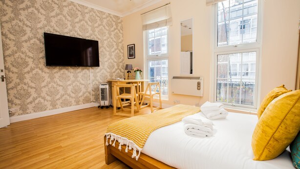 A hotel room with a wooden bed, a flat-screen TV, a desk with a chair, and large windows. - Remarkable Studio Apartment in Central London (London)