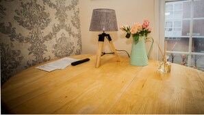 A wooden table with a lamp, a vase with flowers, and papers. - Remarkable Studio Apartment in Central London (London)