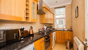 A modern kitchen with wooden cabinets, stainless steel appliances, and a black granite countertop. - Remarkable Studio Apartment in Central London (London)