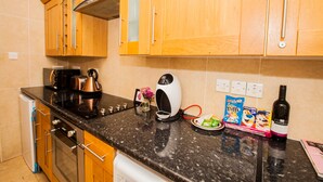 A kitchen with wooden cabinets, a black countertop, a coffee maker, a kettle, a wine bottle, and some cereal boxes. - Remarkable Studio Apartment in Central London (London)