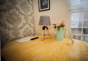A wooden table with a lamp, a vase with flowers, and papers.