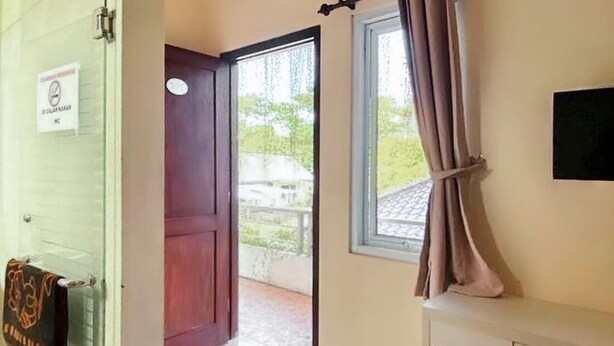 Une pièce avec une porte en bois, une fenêtre avec des rideaux et un téléviseur à écran plat fixé au mur.