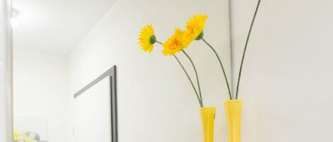 A bathroom with a glass shelf holding yellow towels and two yellow vases with flowers.