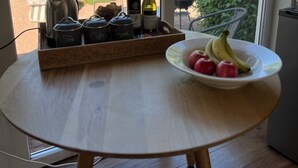 A round wooden table with a tray of tea, sugar, and coffee containers, a bottle of wine, and a bowl of fruit.