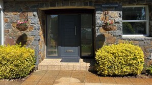 A stone house with a tiled roof, a black front door, and two flower baskets on either side.
