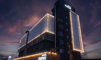 A modern hotel with a prominent 'HOTEL CURVE' sign, large windows, and a flat roof design.