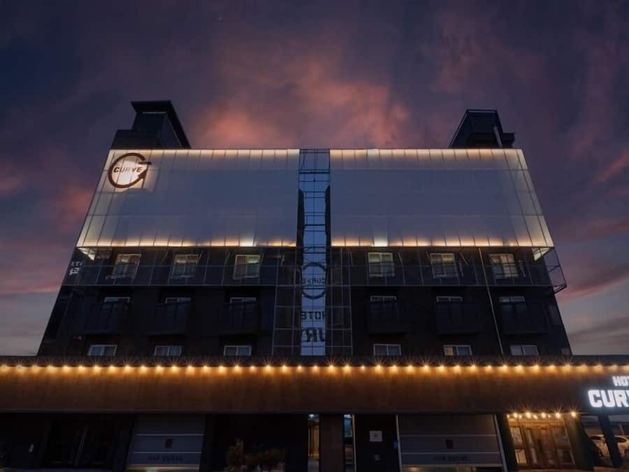 A hotel with a modern design, featuring a prominent 'Curve' sign, multiple floors, and a well-lit facade.