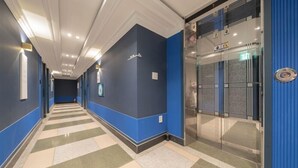 A hotel corridor with blue walls, a checkered floor, and a glass elevator. - CURVE HOTEL IKSAN (Iksan)
