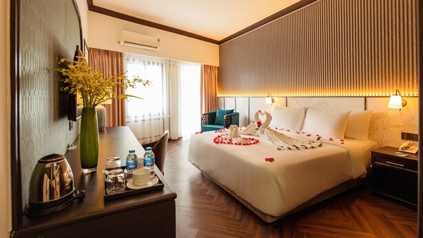 A hotel room with a large bed, bedside table, and a desk with a vase of flowers. - DAI NAM BOUTIQUE HOTEL (Ho Chi Minh City)
