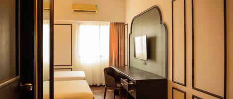 A hotel room with a bed, a desk, a chair, a television, and an air conditioning unit.