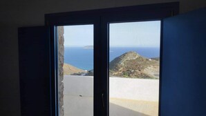 A room with a large window overlooking a mountainous landscape and the sea. - Villa Aigli Anafi (Anafi)