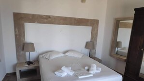 A neatly made bed with white linens and towels, two bedside lamps, a wooden headboard, and a dark wooden wardrobe. - Villa Aigli Anafi (Anafi)
