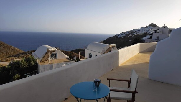 A terrace with a table and chair overlooking a coastal view with white buildings and the sea. - Villa Aigli Anafi (Anafi)