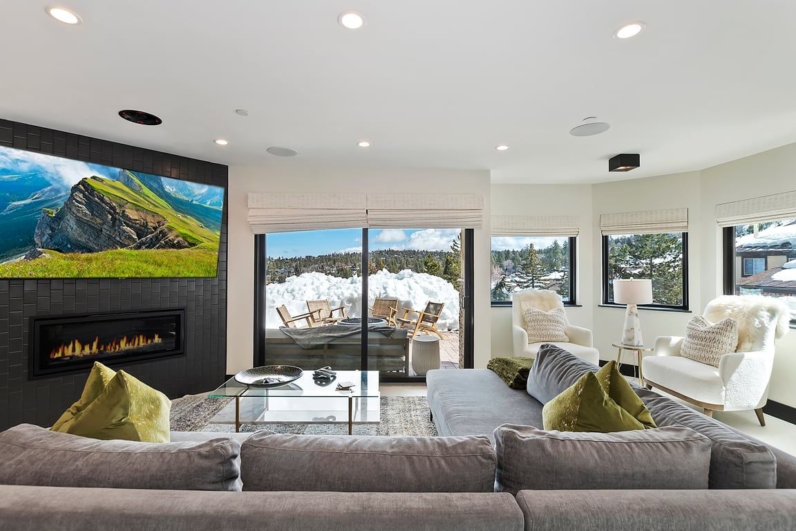 A modern living room with a fireplace, a large TV, and a view of a snowy landscape.