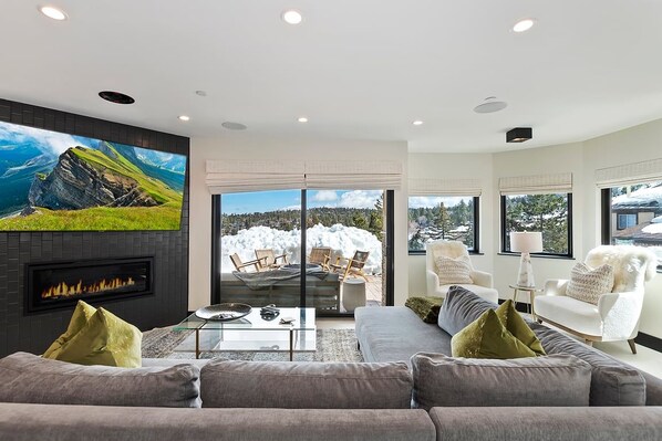 A modern living room with a fireplace, a large TV, and a view of a snowy landscape.