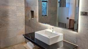 A modern bathroom with a large mirror, a white sink, and a shower area. - River Lumi Resort - Taveta (Chala)