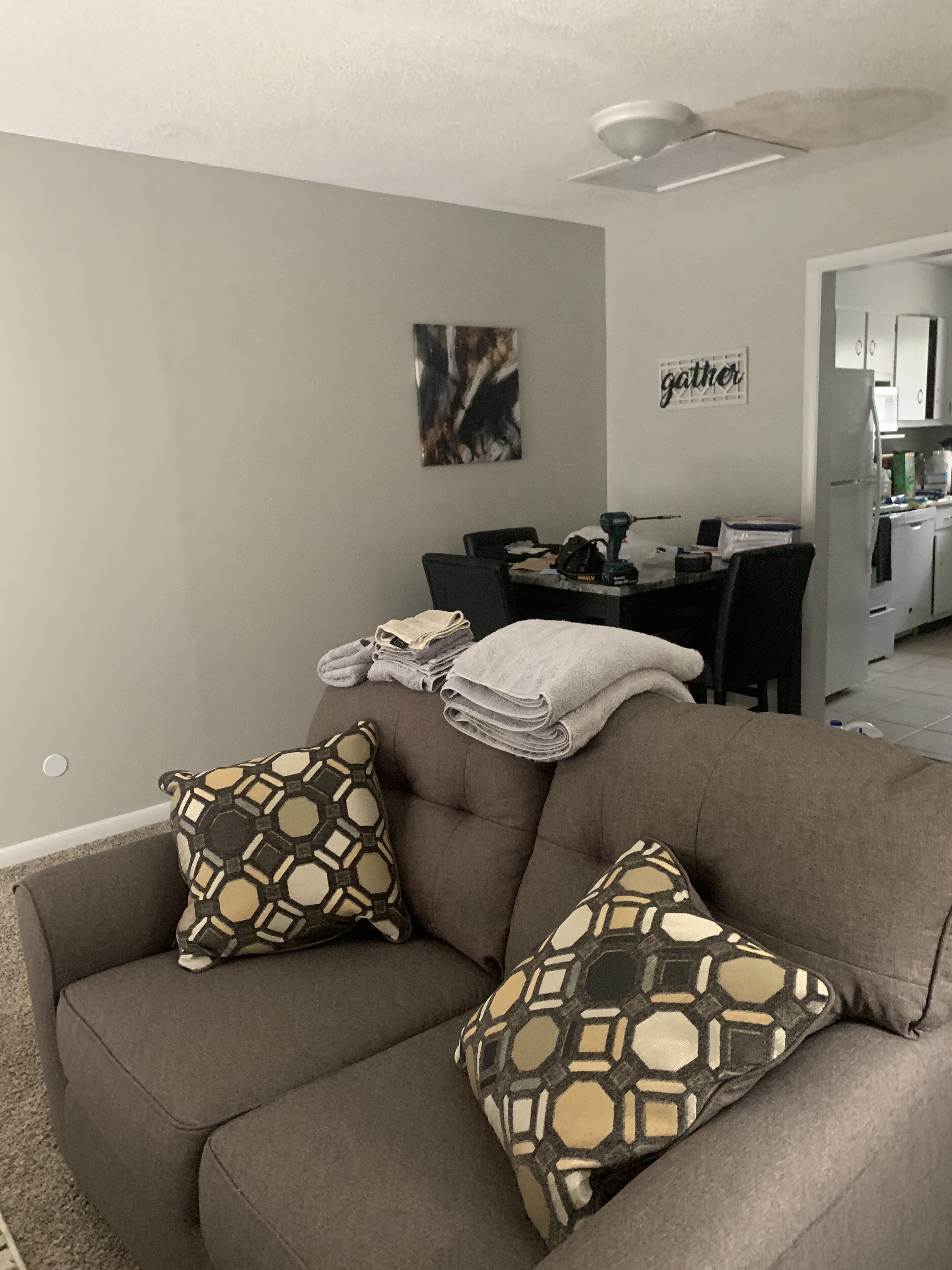 A living room with a gray sofa, patterned throw pillows, a dining area with a table and chairs, and a kitchen in the background.