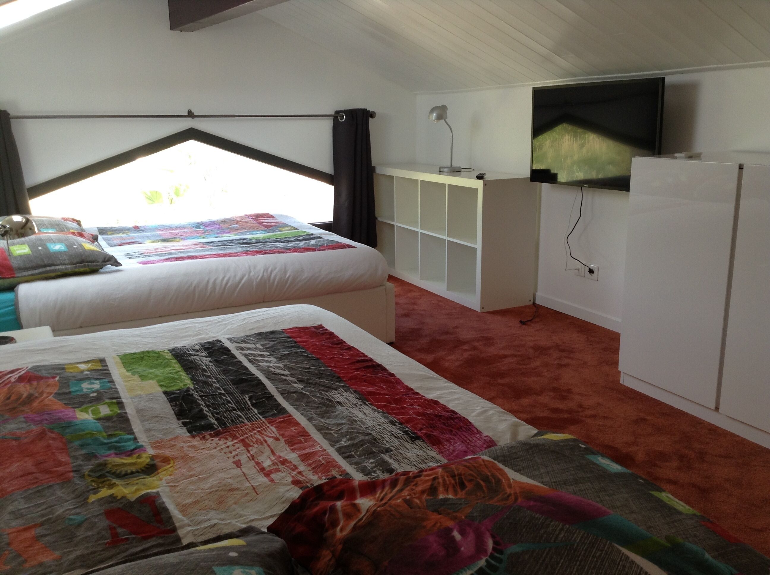 Een slaapkamer met twee bedden, een televisie, een kledingkast en een raam met gordijnen.
