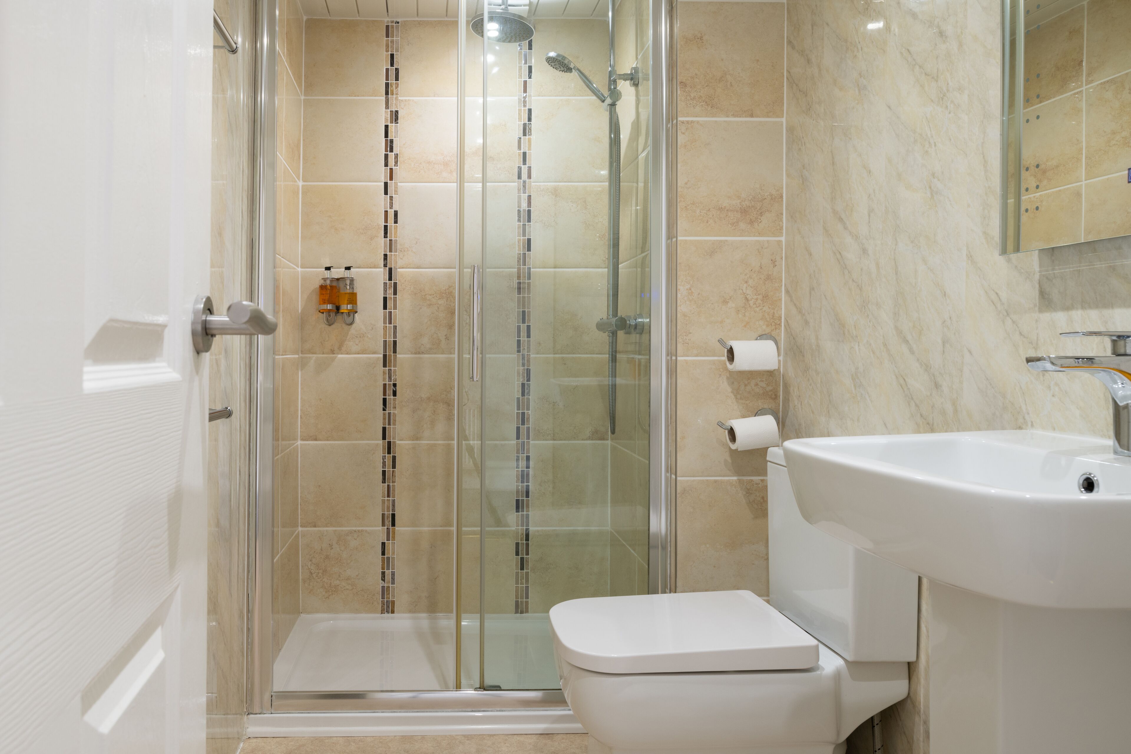 A modern bathroom with a glass-enclosed shower, a white toilet, and a sink with a mirror above it.